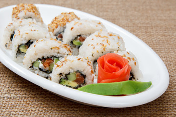 Uramaki sushi rolls with red fish and pickled ginger and piece of avocado on ceramic plate