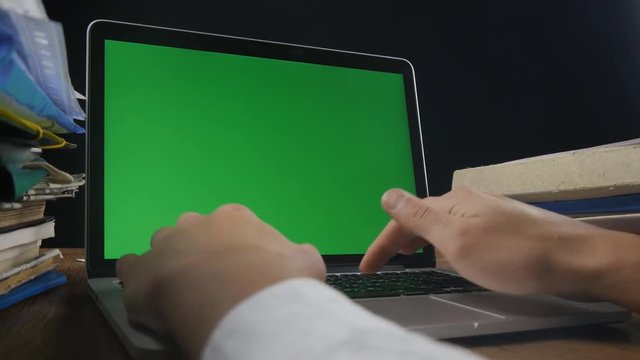 Close up of man works at laptop late ot office with Green Screen. Businessman working at night at the computer with Choma Key.