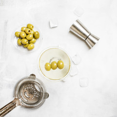 Classic alcoholic cocktail with dry vermouth and green olives, bar tools, gray background, top view