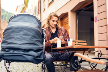 Young Father With Baby Stroller Having Coffee At A Cafe