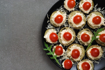 Fried eggplant with cheese, tomatoes, garlic, served on a plate, black background. View from above.