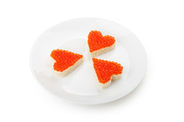 Three sandwiches with red caviar in the shape of heart lie on a white plate isolated on white background.