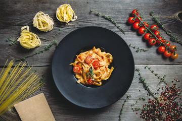 Lenten pasta with cherry tomatoes, basil, thyme and spices. The round black plate on a dark wooden table