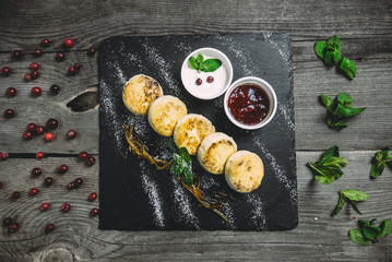 Cheesecakes with lemon peel, jam and sour cream on wooden table