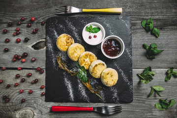 Cheesecakes with lemon peel, jam and sour cream on wooden old table, top view