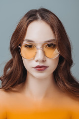 beautiful young girl posing in yellow sunglasses, isolated on grey