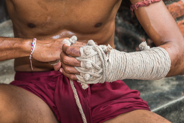 Ancient traditional Muay Thai or Thai boxing fighter putting bandage old style on the hands preparing to fight
