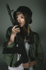 Fototapeta premium attractive young girl in military helmet with rifle, on grey with shadows