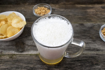 Mug with foam beer, chips and nuts on a wooden background.