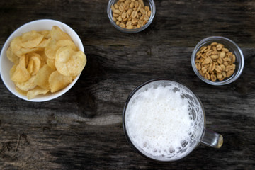 Mug with foam beer, chips and nuts on a wooden background.