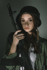 Fototapeta premium beautiful young woman in military helmet with rifle, on grey with shadows