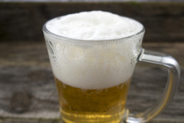 Mug with a frothy beer close-up on a wooden background.