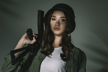 Fototapeta na wymiar attractive girl in military helmet with rifle, on grey with shadows