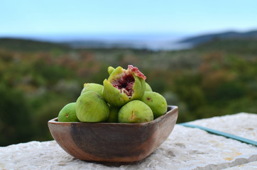 Wooden bowl with fresh, sweet, juicy figs with a Mediterranean landscape in a background