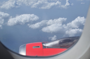 View through airplane window to its engine and clouds in distance during the flight