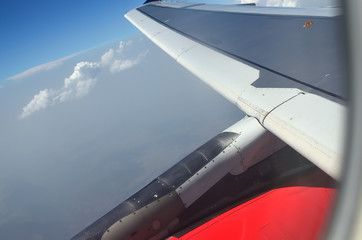 View from a plane to its wing and part of an engine during the flight above the clouds