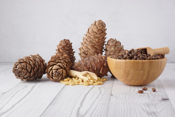 Pine nuts in a bamboo bowl next to cedar cones on a light background