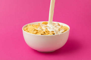close-up view of fresh milk pouring into bowl with corn flakes isolated on pink