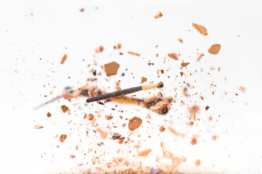 crushed cosmetic powder with makeup brushes falling isolated on white