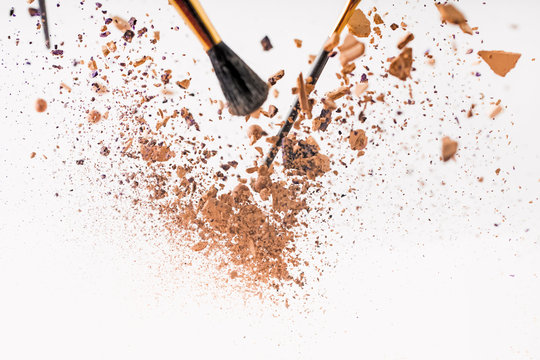 pieces of cosmetic powder with brushes falling isolated on white