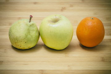 Three different fresh Mediterranean fruits, pear apple and orange, on a wooden background