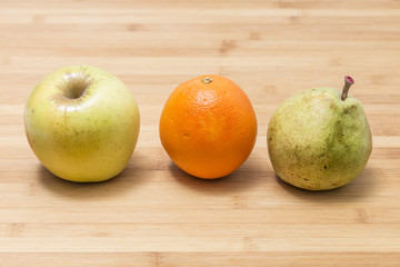 Three different fresh Mediterranean fruits, pear apple and orange, on a wooden background