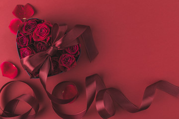 top view of roses in heart shaped gift box with ribbon and petals isolated on red, st valentines day holiday concept