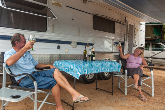 Retired couple sitting under awning of a large caravan toasting retirement.