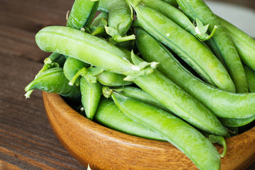Pods of green peas in a wooden bowl.