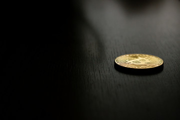 Golden bitcoin coin on the black wooden table. Close up (macro) with black background.