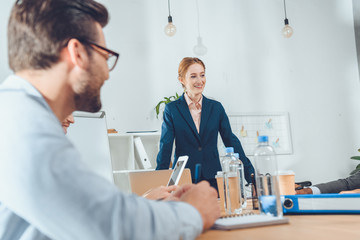 Fototapeta premium businesswoman in formal suit standing against table and speaking to team at office space