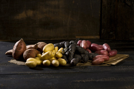Different sorts of potatoes on brown paper, jute and dark wood