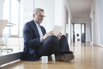 Successful businessman sitting on floor, using digital tablet in his office