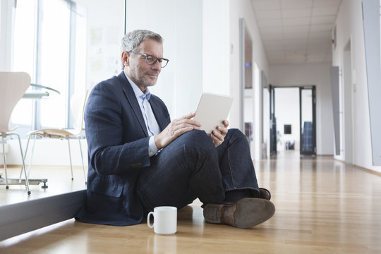 Successful businessman sitting on floor, using digital tablet in his office