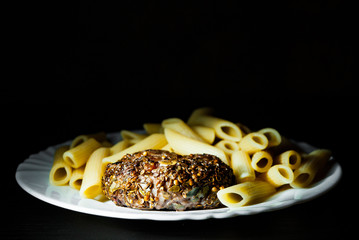 beef meat burger steak cutlets beefsteack with penne pasta on white plate on dark wooden background