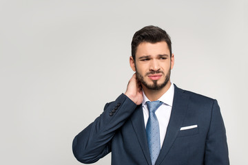 young businessman suffering from pain in neck and looking away isolated on grey