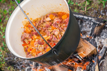 Boiling, hot goulash soup with meat, paprika, potatoes, onion, carrots is the traditional dish of Hungarian cuisine. Meat stew being prepared in crock pot on open fire. Picnic at the weekend in nature