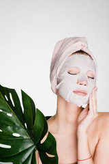 attractive beautiful girl with a towel on her head looks after her face, on her face a tissue mask