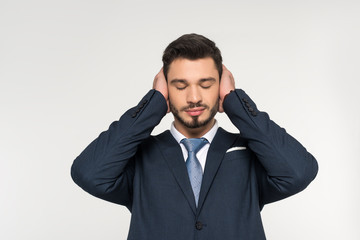 relaxed young businessman with closed eyes closing ears with hands isolated on grey