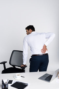young businessman suffering from backache while leaning at chair in office