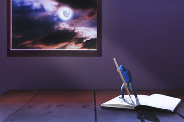 tiny man writing heart on book among light of full moon