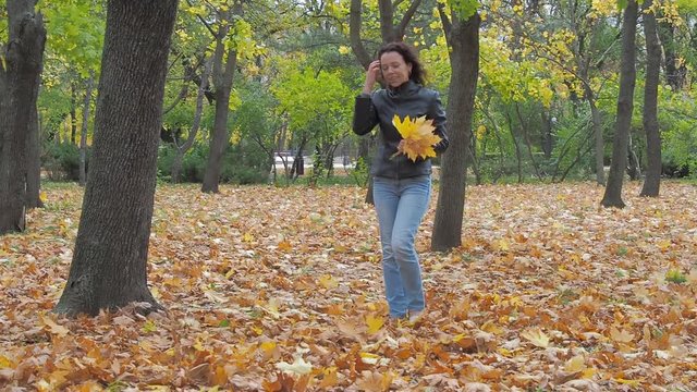 A woman in an autumn park collects yellow leaves.