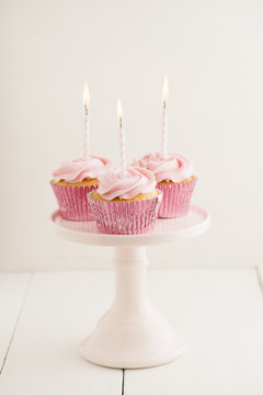 Three pink cup cakes with lighted birthday candles on a cake stand