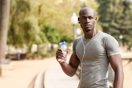 Young black man drinking water before running in urban background