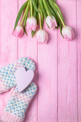 Knitted gloves, wooden pink heart and pink tulips on a wooden background. Valentine's Day background. Top view, free space