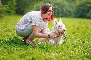 Smiling young woman in grey pants and t-shirt with dog in park
