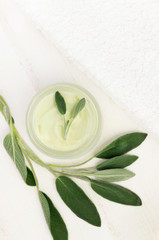 Herbal body and beauty care, spa cosmetics - jar of cream top view framed green Salvia leaves, empty space white wooden table with towel. 