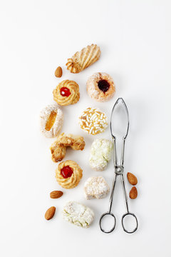 Different sorts of Italian almond cookies, pastry tong and almonds on white background