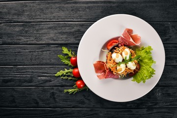 Salad with prosciutto, quail eggs, prunes and fresh vegetables on the plate. On a wooden background. Top view. Free space for text.
