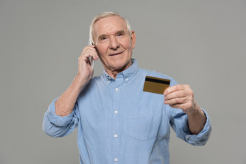 Senior man making a phone call and holding credit card isolated on gray background
